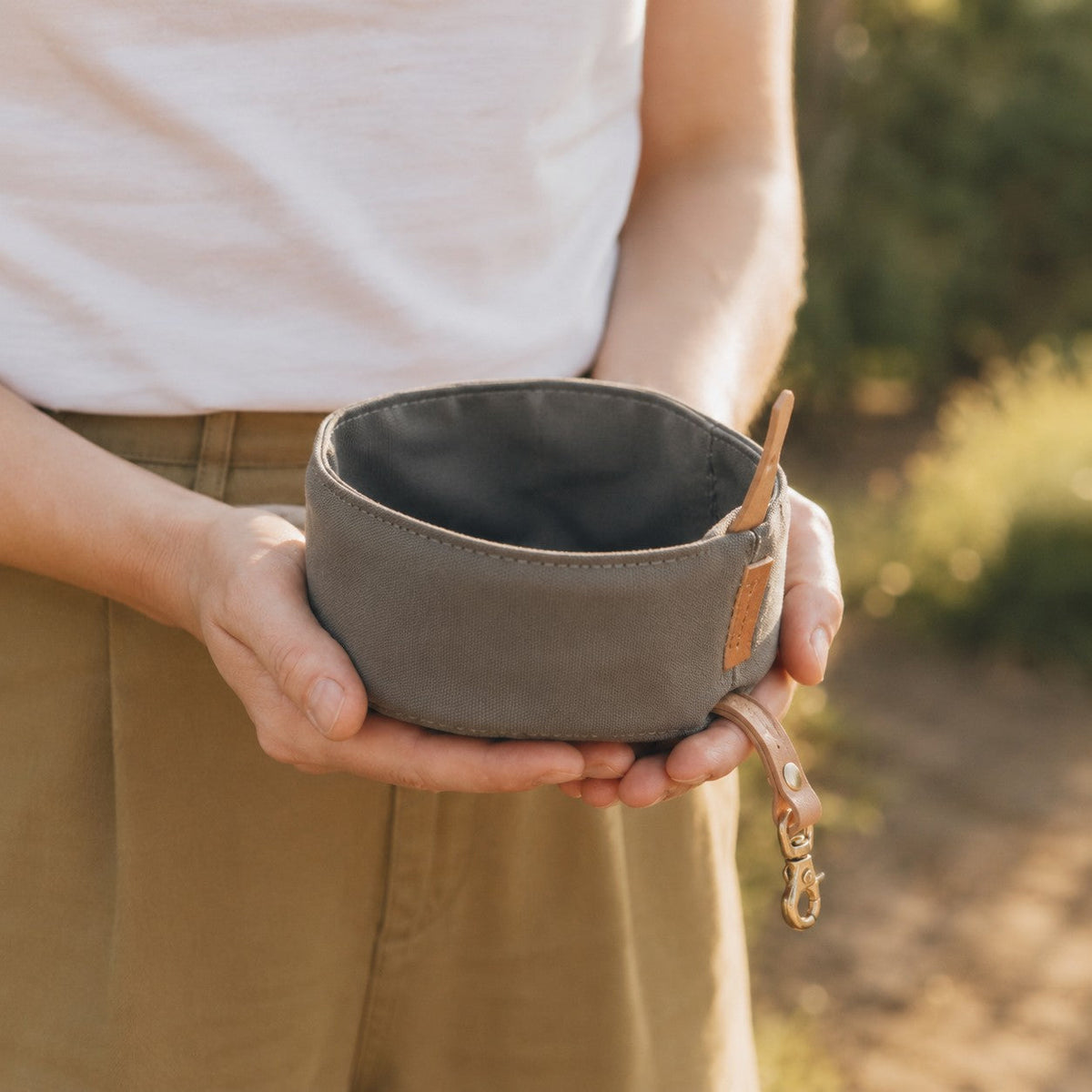 Person holding a gray TrailFold foldable travel dog bowl outdoors